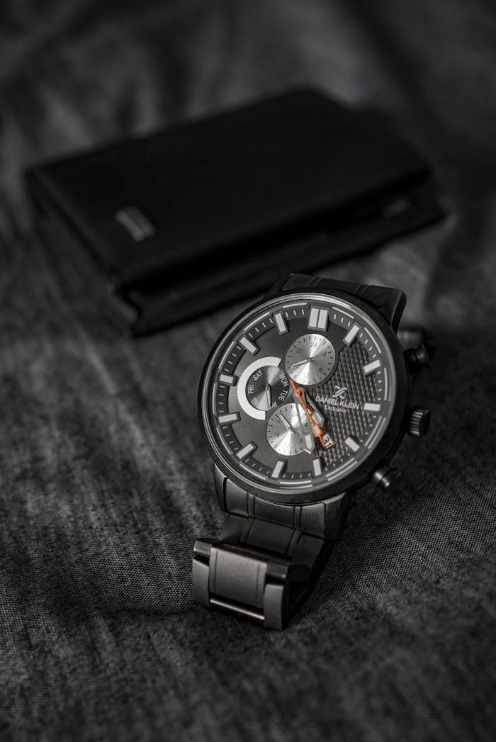 Close-up of a black wristwatch with metallic dial on a textured fabric background.